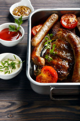 Grilled pork ribs and sausages served with tomato and sauces on wooden table.