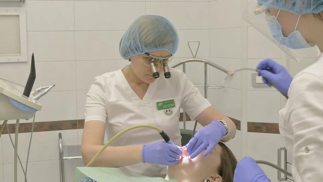 Woman at dentist clinic gets dental treatment to fill a cavity in a tooth. Dental restoration and composite material polymerization with UV light and laser. The doctor works with an assistant.
