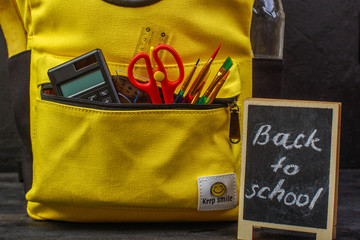 Yellow school backpack with accessories on black background