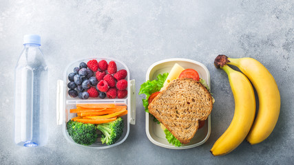 School lunch box with sandwich vegetables water almonds and fruits on grey table healthy