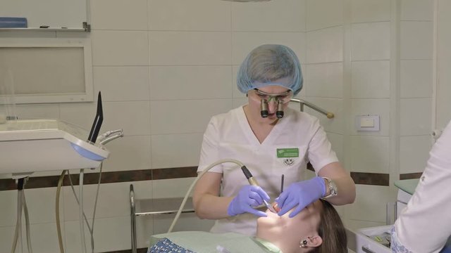 Woman at dentist clinic gets dental treatment to fill a cavity in a tooth. Dental restoration and composite material polymerization with UV light and laser. The doctor works with an assistant.