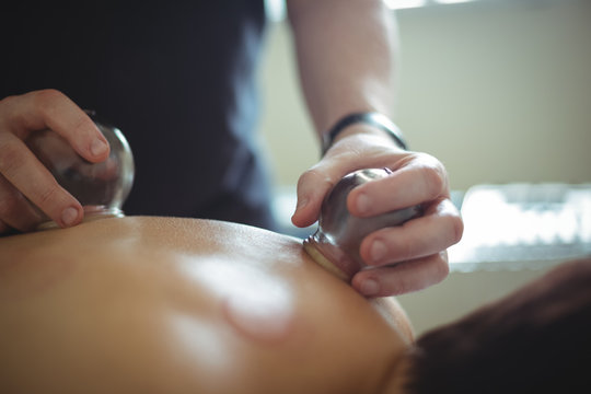 Mid section of therapist giving cupping therapy to man