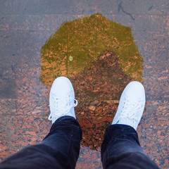 reflection of man with yellow umbrella in white sneakers in puddle