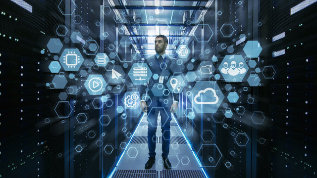 Curios IT Engineer Standing in the Middle of a Working Data Center Server Room. Cloud and Internet Icon Visualisation in the Foreground.