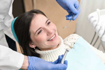 Smiling beautiful girl sitting in a dentist chair is drilling teeth
