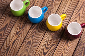 Row of colored empty ceramic clean mugs on old worn brown wooden table with copy space