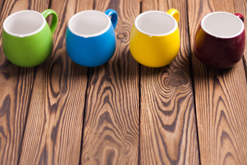 Row of colored empty ceramic clean mugs on old worn brown wooden table with copy space