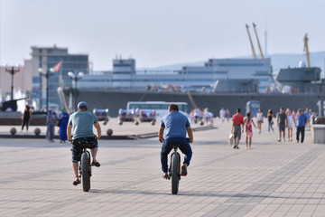 Obraz premium Two men ride bicycles with large wheels and plump tires, the view from the back