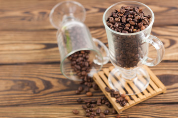 Lot of fried coffee beans in transparent glass for mulled wine on pallet near coffee beans poured out of glass on old wooden rustic brown table