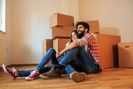 Young couple moving into a new home. They're sitting on the floor in an empty apartment. Real estate concept.	