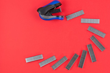 Row of stationery new metal clips and black and blue stapler on red background. Top view