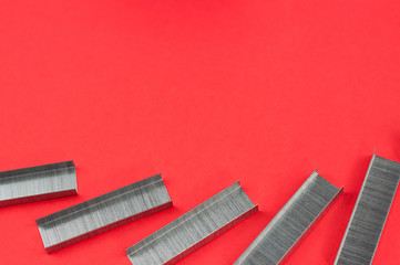 Row of stationery new metal clips for stapler on red background. Top view