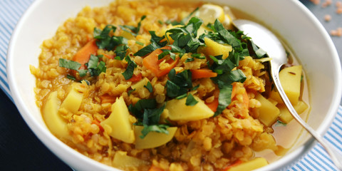 Red lentil stew with potato, carrot and turmeric. Toned photo. Healthy lunch on the round white plate. Colorful vegan dish with potato, carrot and turmeric. European cuisine. Vegetarian.