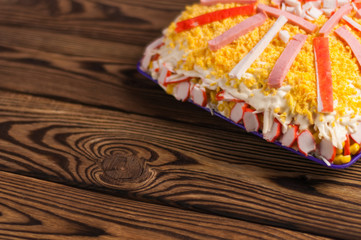 One full violet square plastic plate of prepared salad with potato and crab sticks and egg and sausage and mayonnaise on old rustic weathered wooden table with copy space