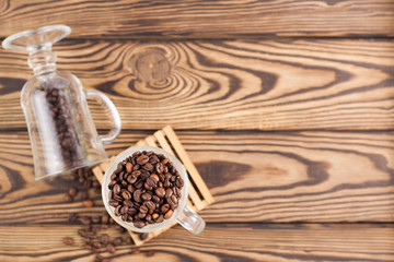 Lot of fried coffee beans in transparent glass for mulled wine on pallet near coffee beans poured out of glass on old wooden rustic brown table
