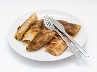 Tasty stuffed cabbage leaf laying on plate on isolated white background, fork and knife on above