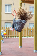 A young girl make a back somersault on the rings in a playgroung, while her hair opens out in the air