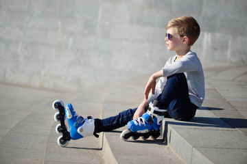 Boy siting with inline roller skates at outdoor skate park