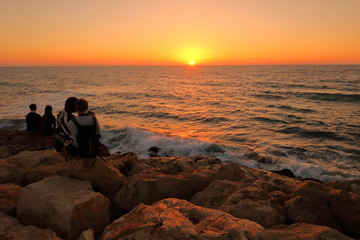 Romantyczny zachód słońca nad morzem, umocnione kamieniami nabrzeże i woda oświetlona złotymi...