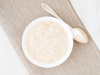 Large bowl of tasty and healthy oatmeal for Breakfast, morning meal. Top view, close up, white wooden rustic table.