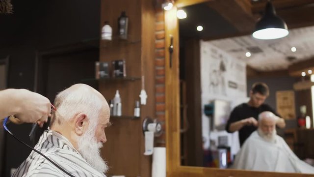 Professional barber makes modern hairstyle fot senior man