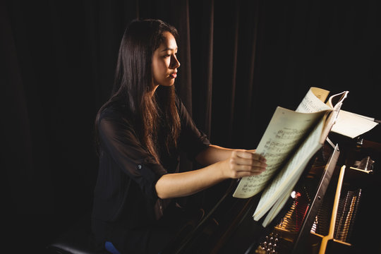 Female student looking at sheet music while playing a piano