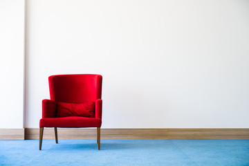 Red chair in white wall interior with blue wood flooring.