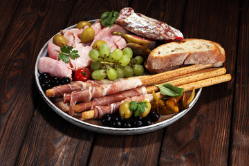 Italian antipasti wine snacks set. Cheese variety, Mediterranean olives, pickles, Prosciutto di Parma, salami and wine in glasses over black grunge background.