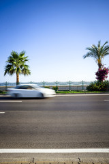 blured moving car drives an empty road palm tree on background