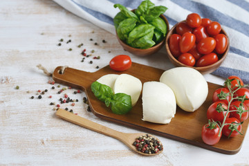 Mozzarella cheese with red tomatoes and basil leaves, pepper, olive oil, wooden desk, healthy food concept
