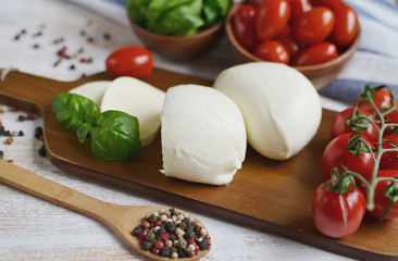 Mozzarella cheese with red tomatoes and basil leaves, pepper, olive oil, wooden desk, healthy food concept