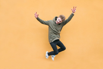 Fototapeta na wymiar Happy young man jumping against the background of an orange wall. The leap of an emotional student on a bright colored background