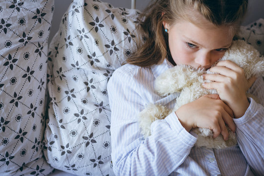 Girl playing with teddy bear on bed