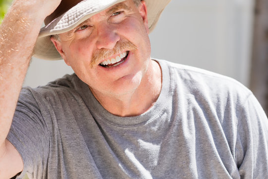 Senior male puts on his cowboy hat on hot sunny day