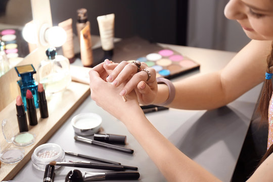 Young woman applying foundation on her hand in makeup room, closeup