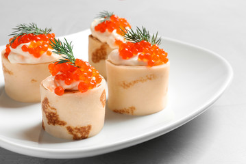 Delicious thin pancakes with red caviar on plate