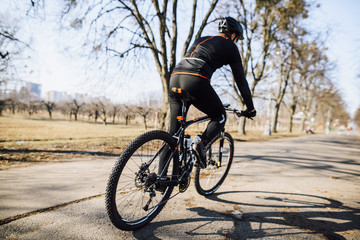 Professional cyclist in black uniform rides on his bicycle on the road in the park