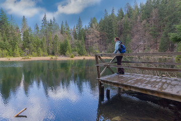 Girl tourist with a backpack on the shore of a forest lake. Travel