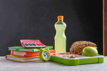 Composition with lunch box and food on table against blackboard