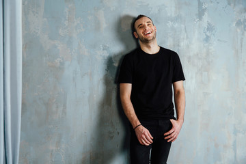 portrait of a young man in a black T-shirt leaned against a vintage gray wall. Copy space.