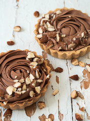 Top view of chocolate tarts served almond nuts on shabby white wooden background