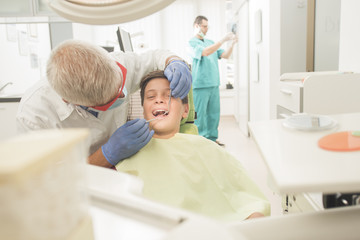 Obraz premium Boy with perfect teeth at the dentist doing check up with the clinic at the background - oral hygiene health care concept