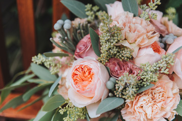 Close up gorgeous wedding bouquet containing eucalyptus and peonies on a brown wooden chair outdoors