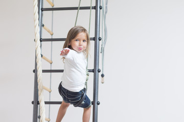 Children Activity Concepts. Little Caucasian Girl Having Stretching Exercises on Wall Bars Indoors.