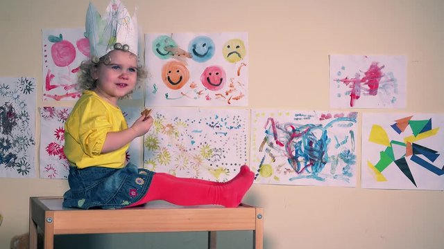 toddler child with paper crown eating cookies sitting on little table