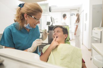 Obraz na płótnie Canvas Boy with perfect teeth at the dentist doing check up with the clinic at the background - oral hygiene health care concept