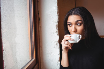 Young woman looking through window while having coffee