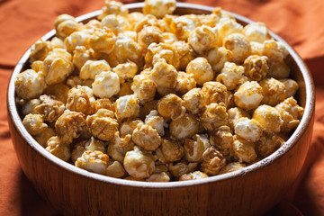 Wooden bowl with sweet popcorn on orange bedding. Snacks and food for a movie