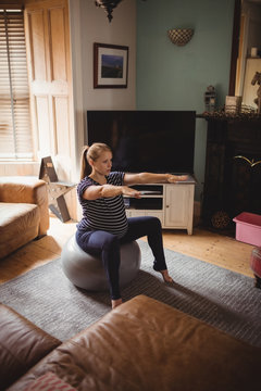 Pregnant woman performing stretching exercise on fitness ball in living room