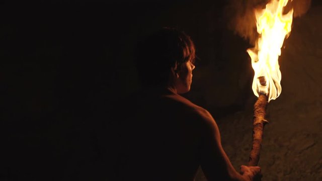 Careful hermit with burning torch in hand walks and looks around in stone cave